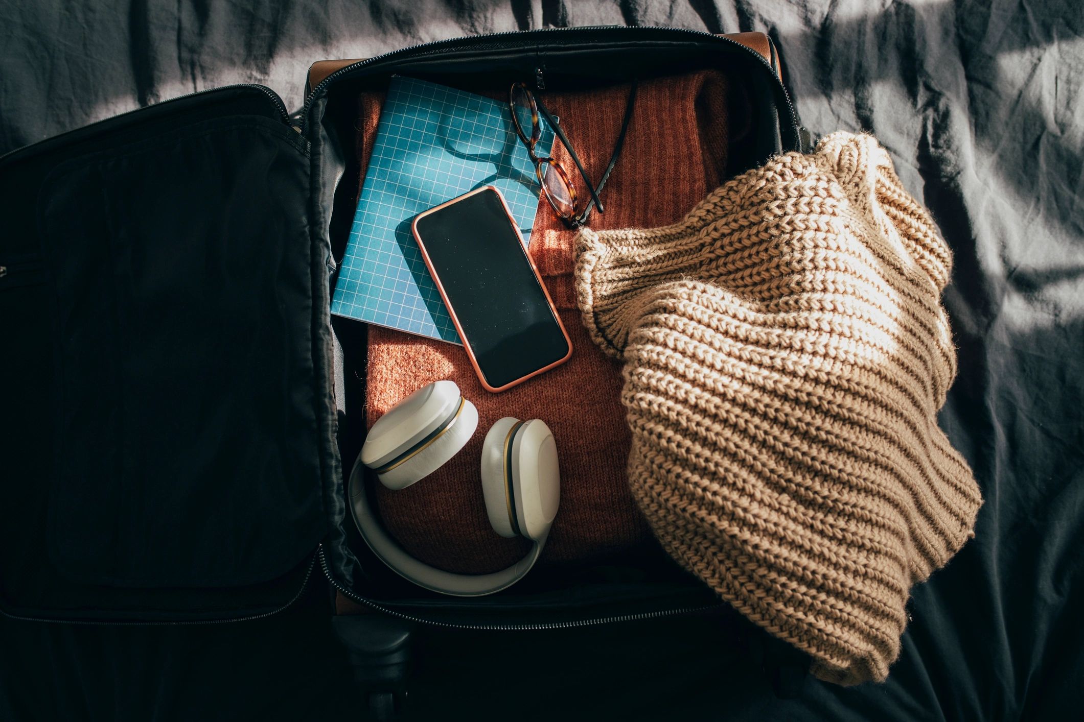 Open suitcase packed with clothes laid out on a bed