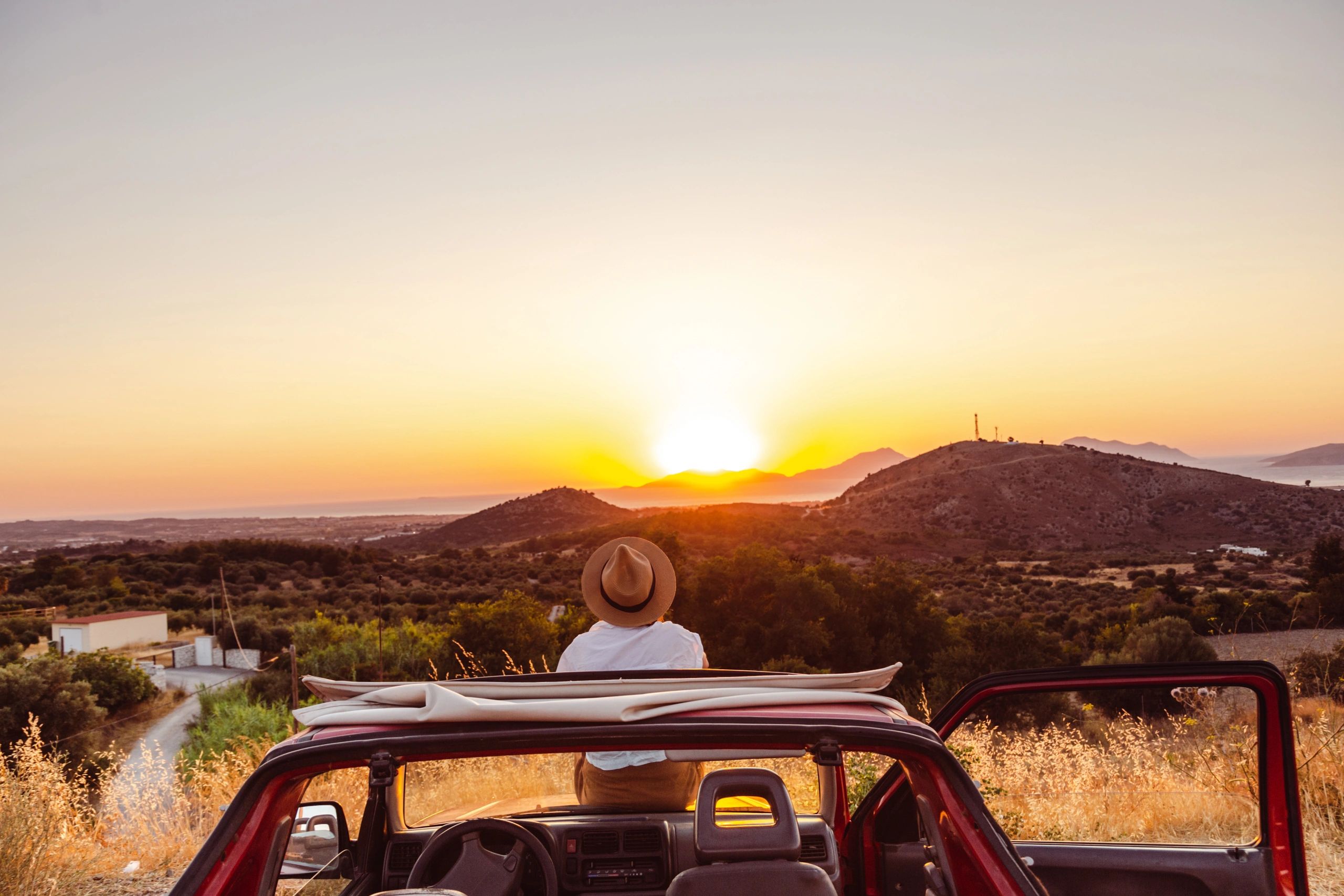 Woman sitting on a car enjoying sunset on a road trip