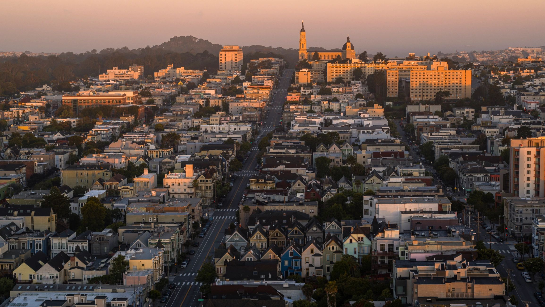Historic church towers rise above Mission District. Residential streets stretch toward Buena Vista Park in San Francisco, California.