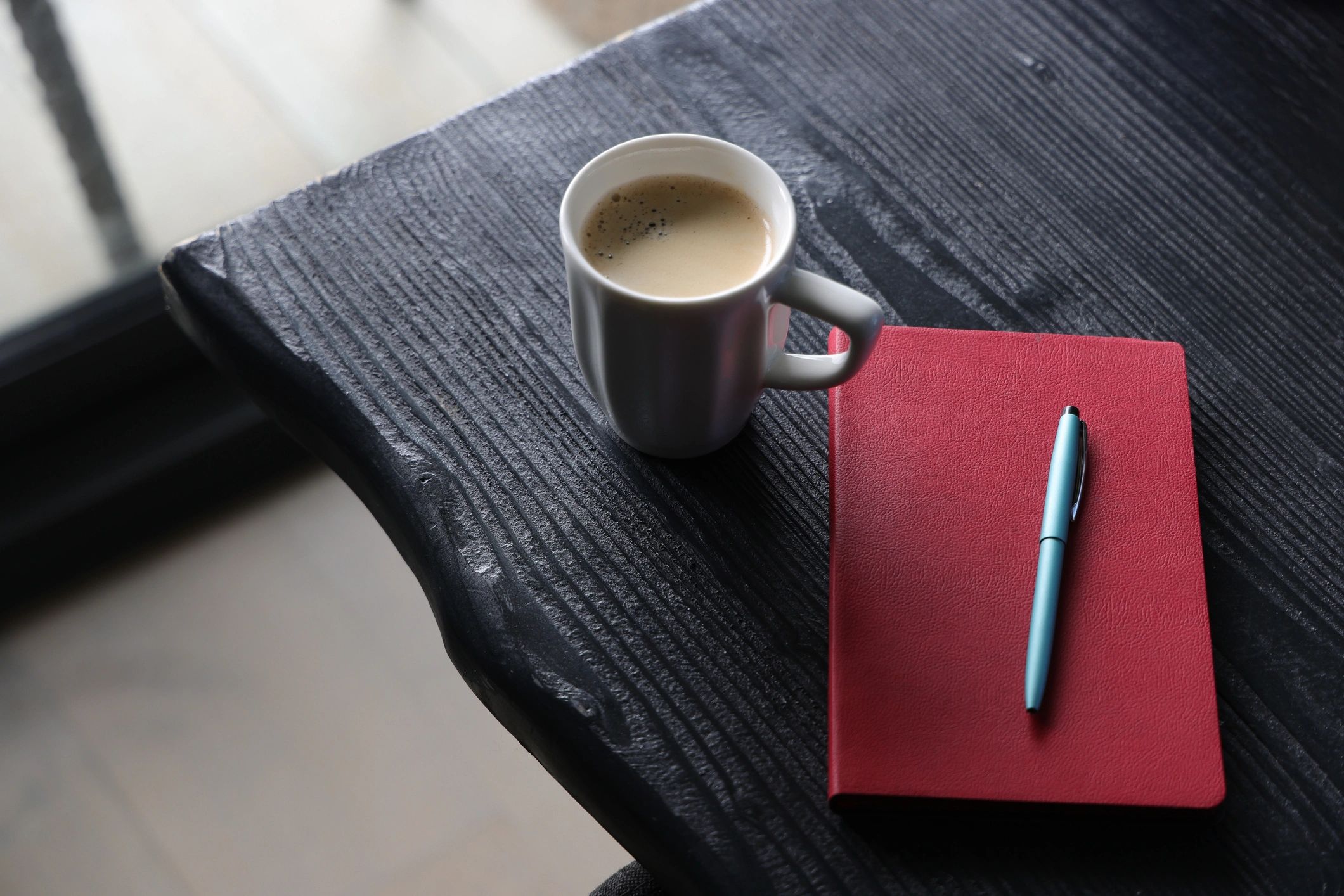 Notebook with pen beside a coffee mug on a dark wooden desk